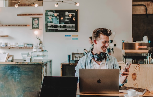 Happy customer by laptop looking at notification on his phone